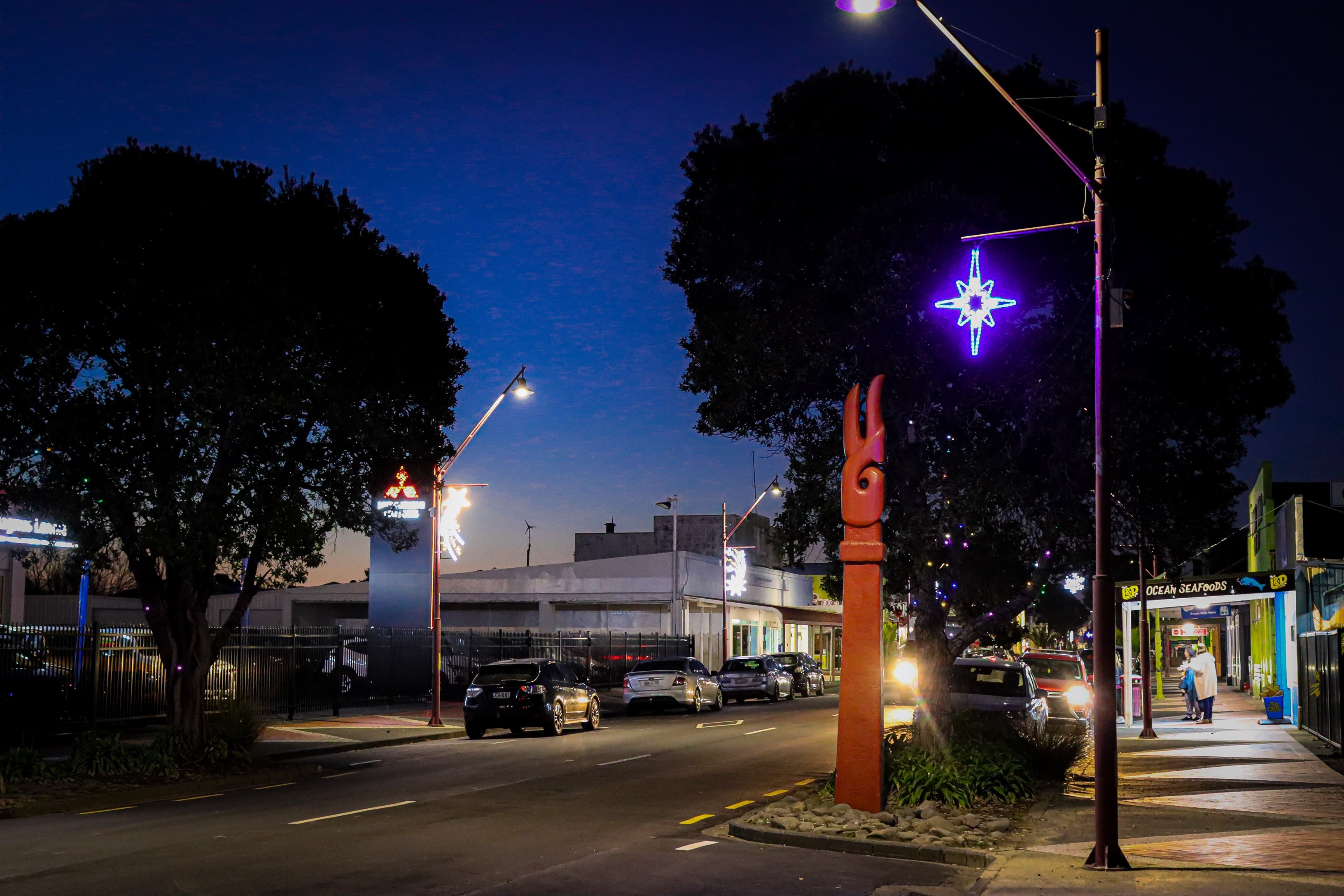 A town street in the evening with blue-black sky and small right neon light in the shape of a snowflake.  