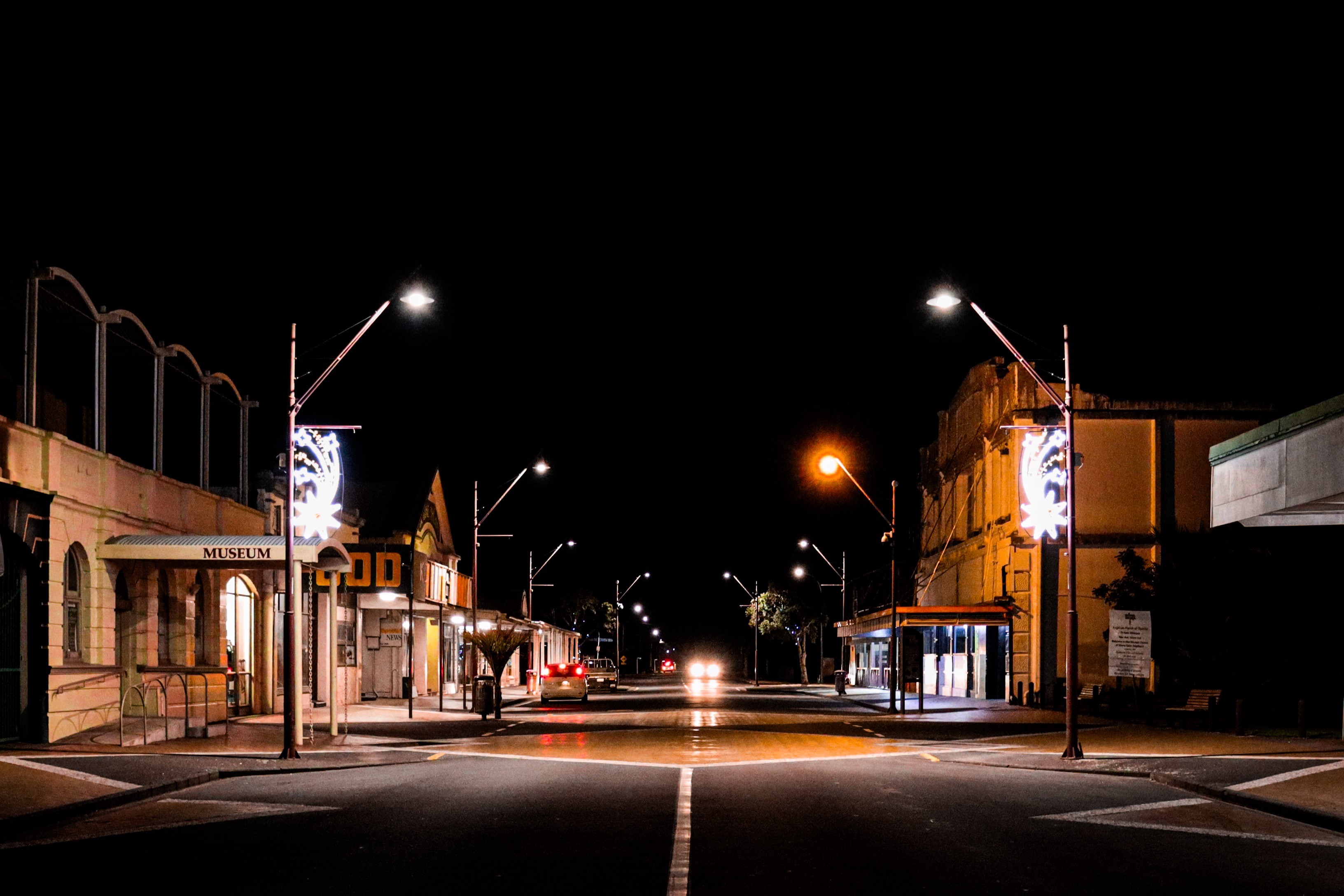 A dark small-town street looking down the middle of the road with bright neon lights on lampposts on either side.  