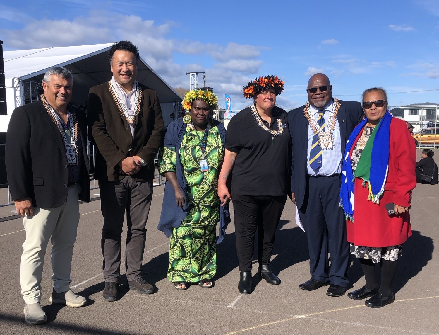 Mayor stands alongside delegation and officials from the Solonman Islands - bright clothing, flower headdress, shell necklaces.