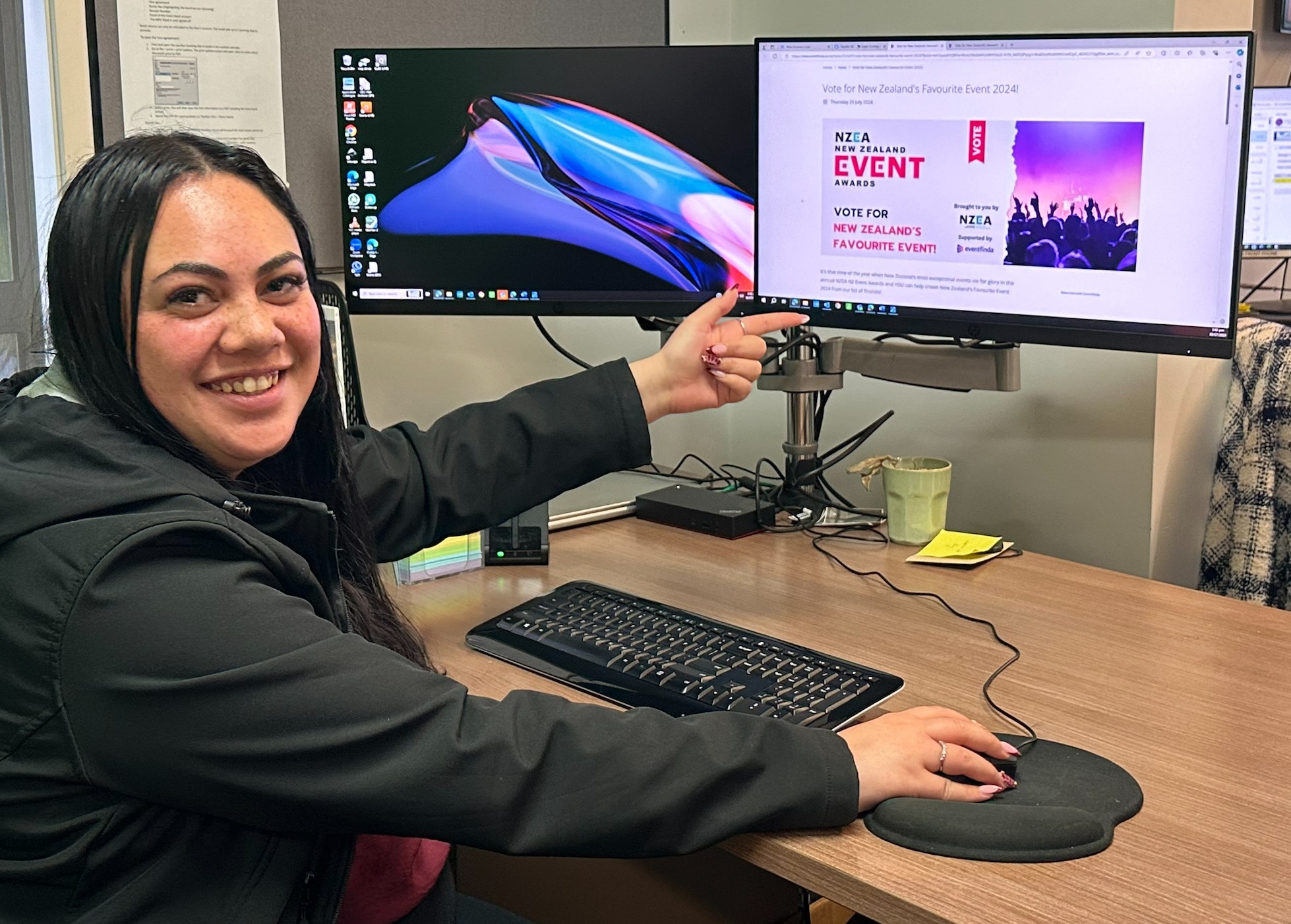 Young lady smiling at camera points to a screen that shows the NZEA voting page.  