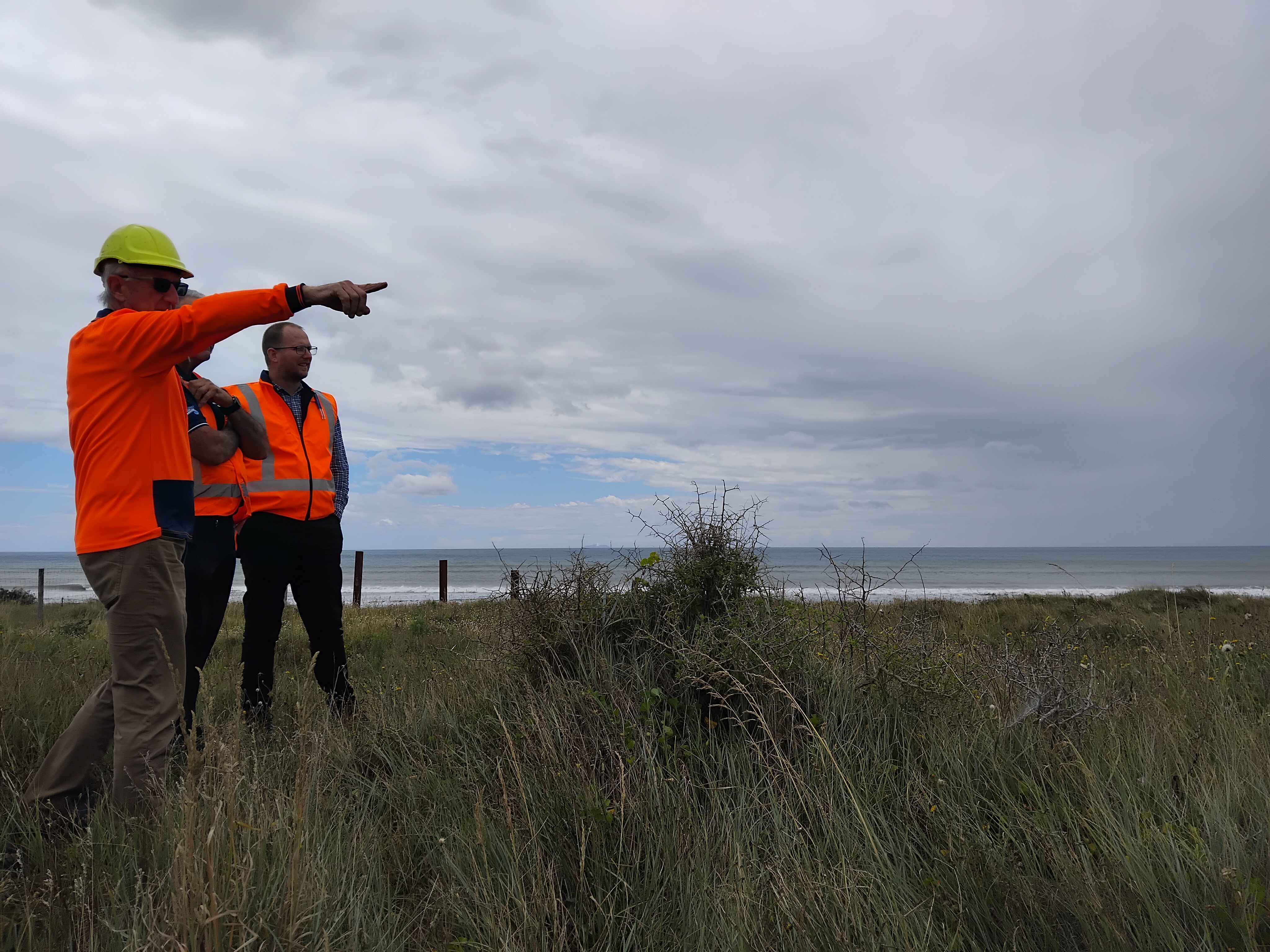 Three men in high-viz looking over the dunes towards the beach discussing the beach access location.